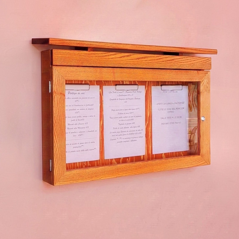 Abschließbarer Speisekartenkasten aus Holz für den Außenbereich an einer rosa Wand montiert.