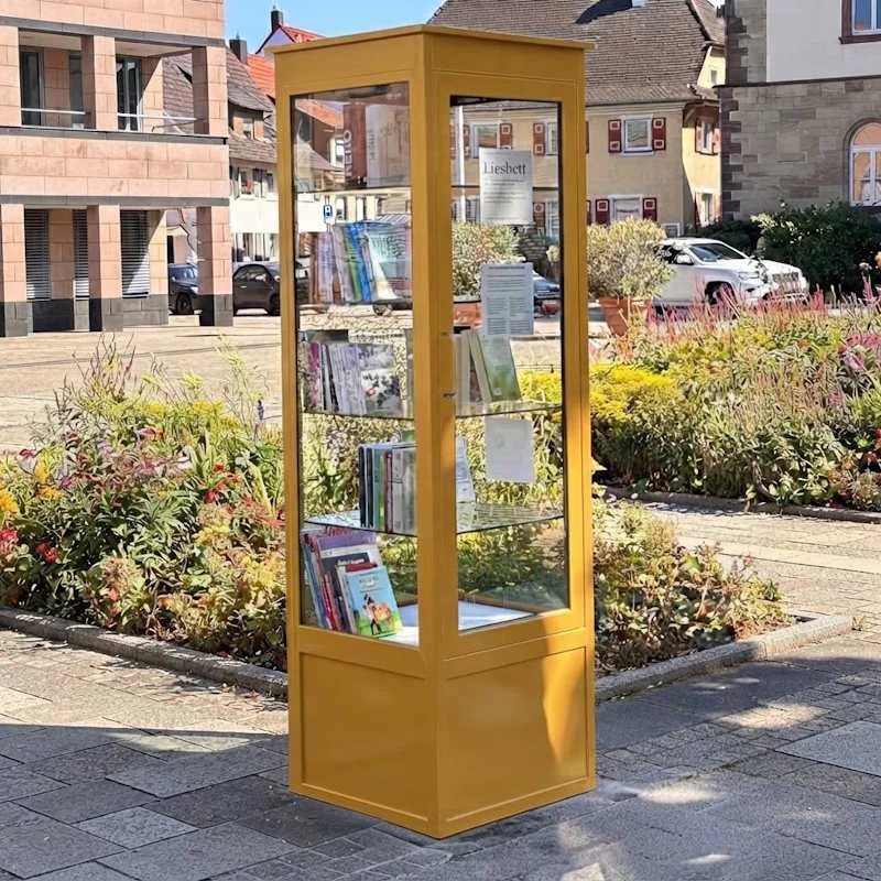 Freistehende Buecherzelle Postgelb aus Metall auf einem oeffentlichen Platz
